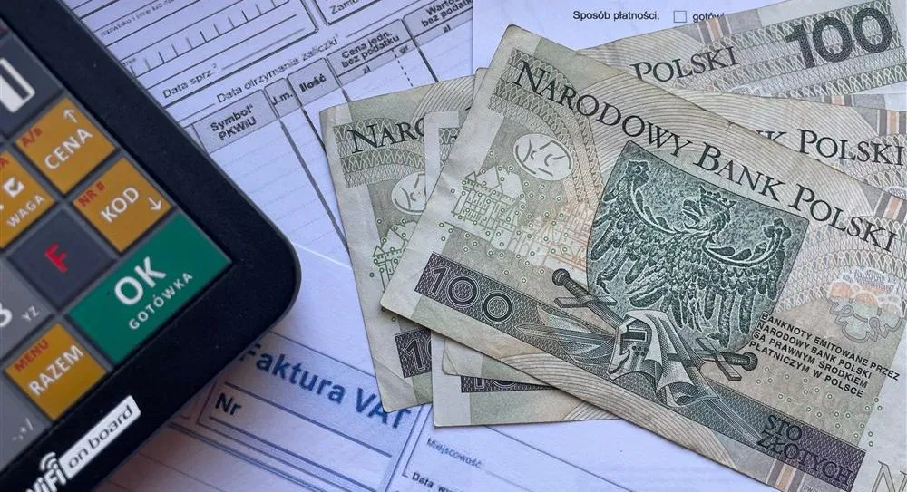 Polskie banknoty obok faktur i kalkulatora, symbolizujące rozliczenie kosztów materiałów